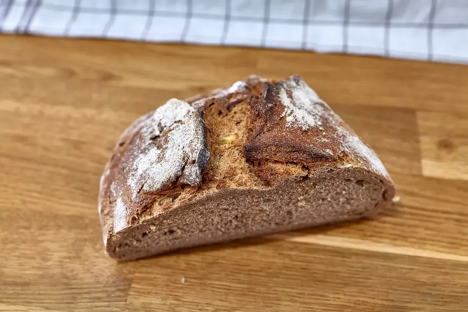 A dark rye loaf with a cracked crust cut open on a board, showing a dense, moist crumb
